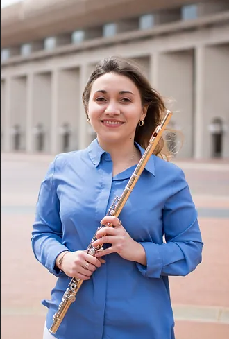 Image of woman in blue shirt holding a flute, smiling, standing outside